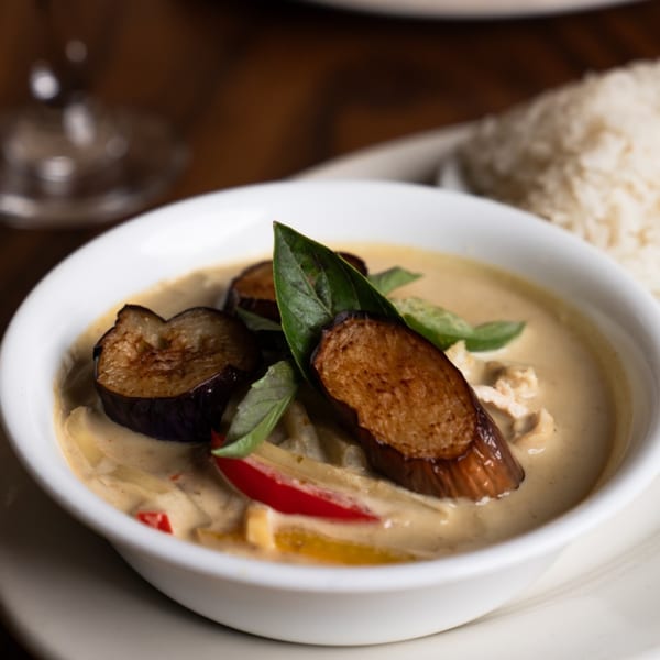 A bowl of Thai green curry with eggplant, bell peppers, and basil, served with rice.