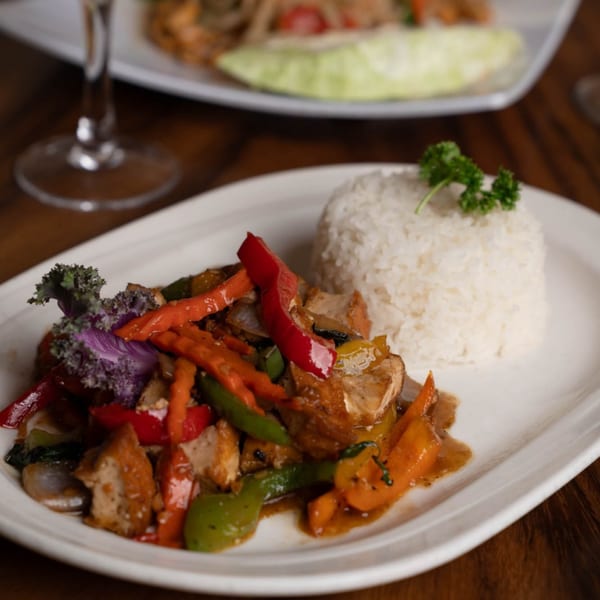 Thai stir-fried chicken with colorful vegetables and white rice on a white plate.