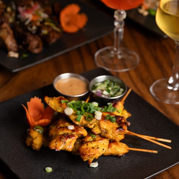 Grilled chicken satay skewers with peanut sauce and cucumber relish, garnished with scallions.