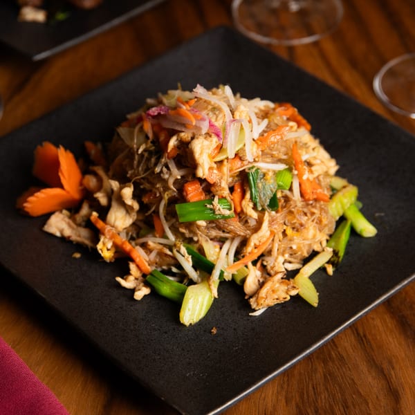Thai One On's glass noodle stir-fry with chicken, carrots, and green onions on a black plate.