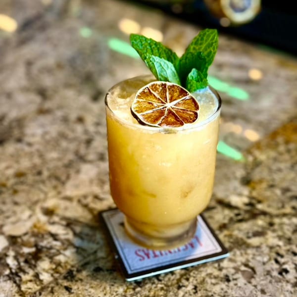 A Thai One On cocktail, garnished with a dried lime slice and fresh mint, on a granite counter.