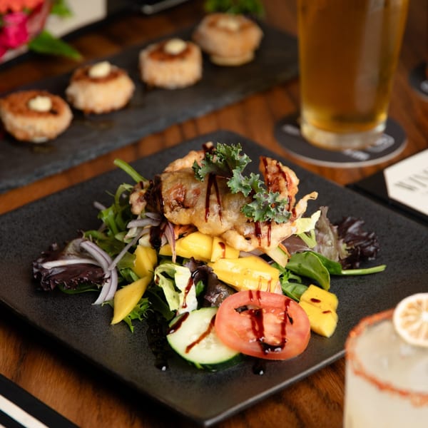Soft shell crab salad with mango, tomato, cucumber, and greens, drizzled with sauce.