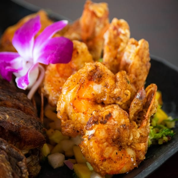 Crispy fried shrimp and fish with a purple orchid garnish on a dark plate at Thai One On.